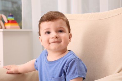 Cute baby boy sitting in armchair at home