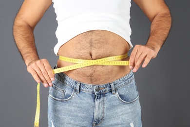 Overweight man with measuring tape on gray background, closeup