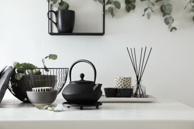 Stylish black teapot and beautiful green eucalyptus leaves on white table indoors