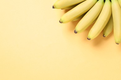 Bunch of ripe baby bananas on light orange background, top view. Space for text