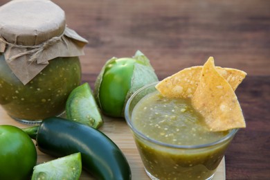Photo of Delicious salsa sauce with tortilla chips and ingredients on wooden table, closeup