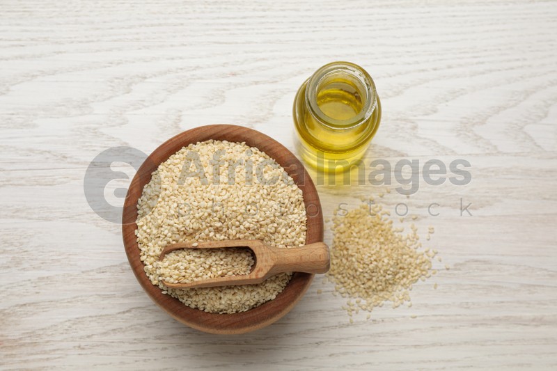 Fresh sesame oil and seeds on white wooden table, flat lay