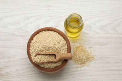Fresh sesame oil and seeds on white wooden table, flat lay