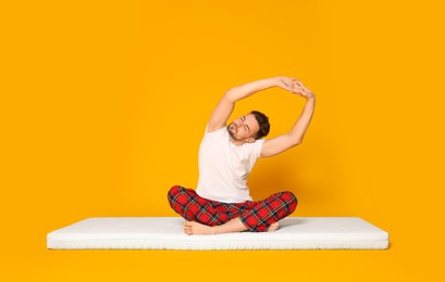 Man sitting on soft mattress and stretching against orange background