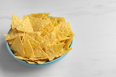 Photo of Tortilla chips (nachos) in bowl on white table. Space for text