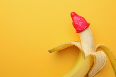 Banana with condom on orange background, top view and space for text. Safe sex concept