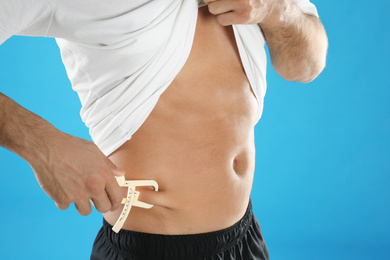 Man measuring body fat layer with caliper on light blue background, closeup. Nutritionist's tool