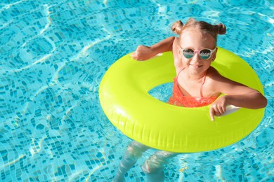 Photo of Happy little girl with inflatable ring in outdoor swimming pool on sunny day, space for text