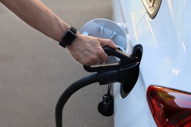 Man inserting plug into electric car socket at charging station, closeup