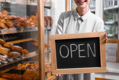 Photo of Female business owner holding OPEN sign in bakery, closeup