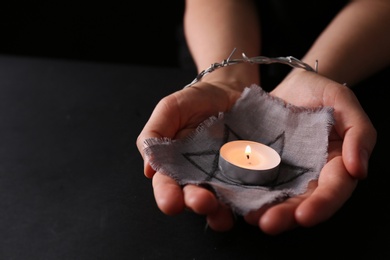 Woman tied with barbed wire holding star of David and burning candle on black background, closeup. Holocaust memory day