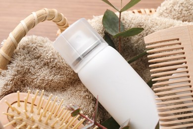 Dry shampoo spray, towel and hairbrushes with eucalyptus branch in basket on table, closeup