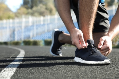 Sporty man tying shoelaces before running at stadium