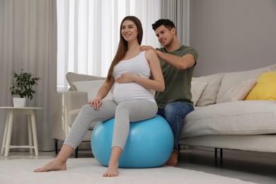 Husband massaging his pregnant wife in light room. Preparation for child birth