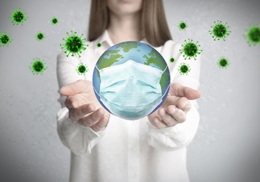 Image of Woman holding Earth with medical mask on light background, closeup. Concept of coronavirus outbreak