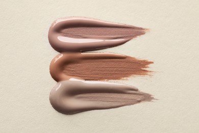 Different shades of liquid foundation on beige background, top view