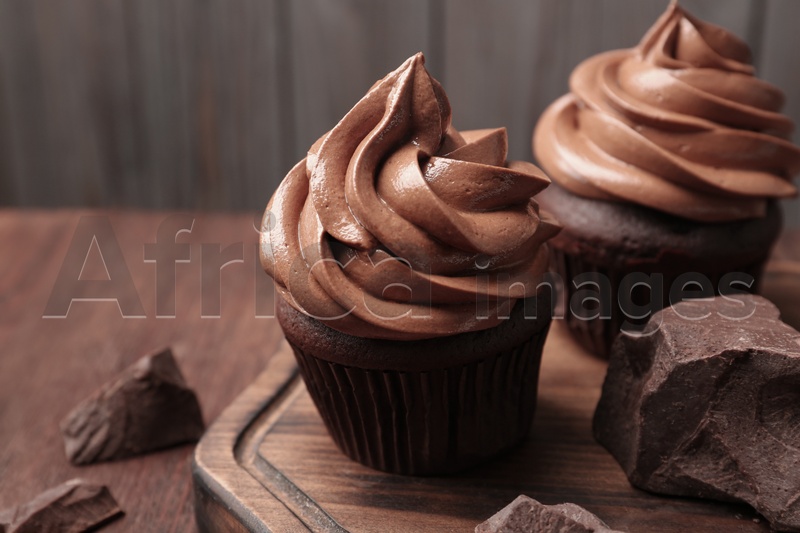Delicious cupcakes with cream and chocolate pieces on wooden table, closeup
