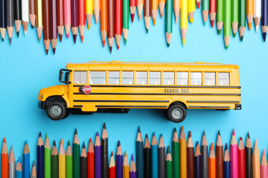 Flat lay composition with yellow school bus model on light blue background. Transport for students