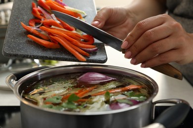Photo of Woman putting cut vegetables into pot with delicious bouillon on stove in kitchen, closeup