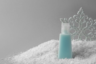 Photo of Winter skin care. Hand cream and decorative snowflake on artificial snow against light grey background, space for text