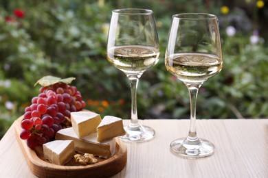 Photo of Glasses of white wine and snacks served on wooden table outdoors