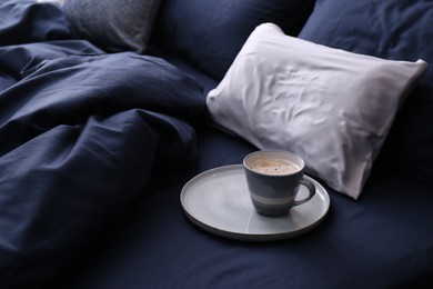 Photo of Cup of coffee on bed with stylish silky linens