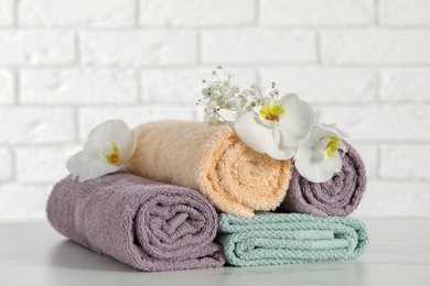 Rolled and folded towels with lilies on white table, closeup