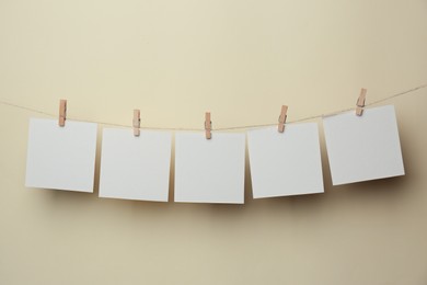 Wooden clothespins with blank notepapers on twine against beige background. Space for text