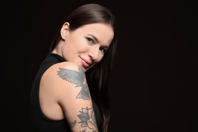 Beautiful woman with tattoos on arm against black background. Space for text