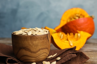 Bowl of raw unpeeled pumpkin seeds on wooden table against blue background. Space for text