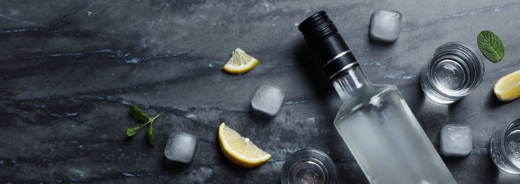 Image of Bottle of vodka, shot glasses, lemon, mint and ice on black marble table, flat lay. Space for text. Banner design