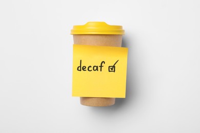 Note with word Decaf and checkbox attached to takeaway coffee cup on white background, top view