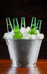 Metal bucket with bottles of beer and ice cubes on wooden background