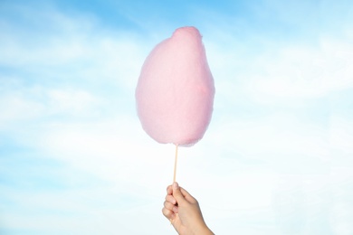 Photo of Woman holding sweet pink cotton candy on blue sky background, closeup view