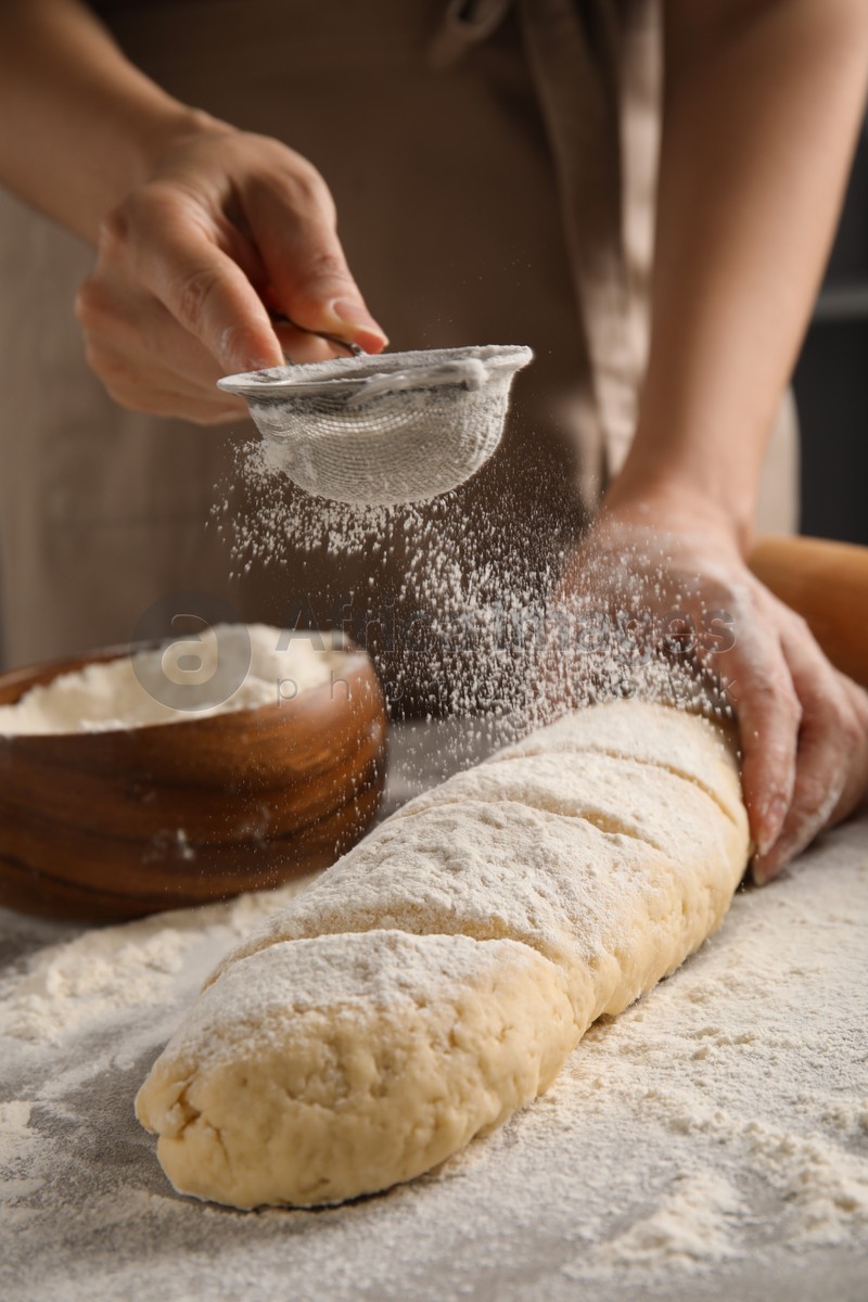 Woman pouring flour onto loaf of raw bread at table, closeup