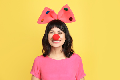 Photo of Joyful woman with large bow and clown nose on yellow background. April fool's day