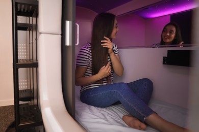 Happy young woman sitting in capsule of pod hostel