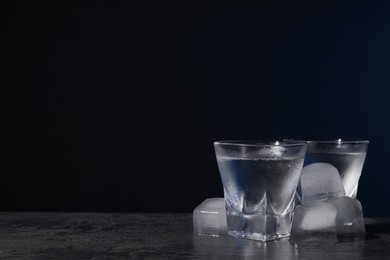 Vodka in shot glasses with ice on black table against dark background. Space for text