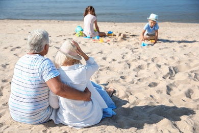 Little children playing on sea beach, focus on grandparents