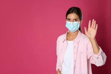 Woman in protective mask showing hello gesture on pink background, space for text. Keeping social distance during coronavirus pandemic