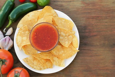 Photo of Tasty salsa sauce with tortilla chips and ingredients on wooden table, flat lay. Space for text