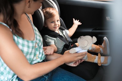 Photo of Woman with knitted toy near her daughter in child safety seat inside car