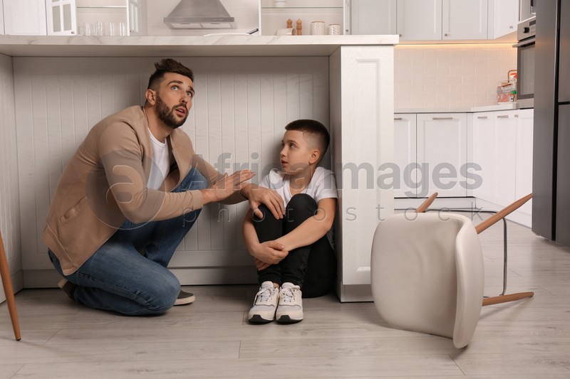 Father and his son hiding under table in kitchen during earthquake