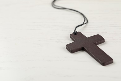 Christian cross on white wooden table, closeup. Space for text