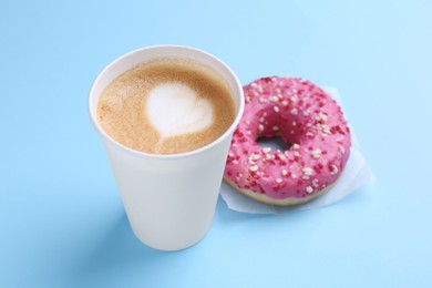 Photo of Tasty frosted donut and paper cup of coffee on light blue background