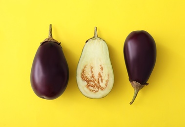 Cut and whole raw ripe eggplants on yellow background, flat lay