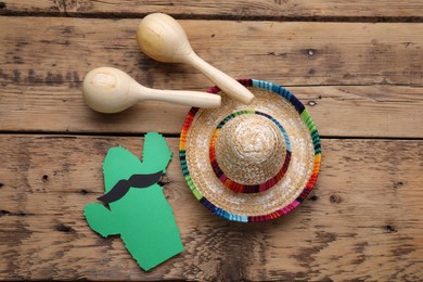 Photo of Maracas, paper cactus with mustache and sombrero hat on wooden table, flat lay. Musical instrument