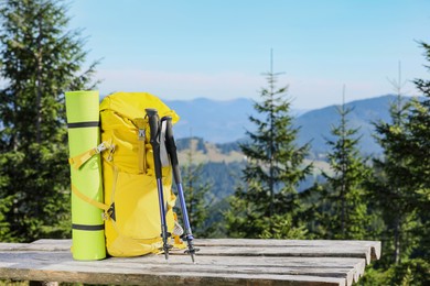 Backpack, sleeping mat and trekking poles on wooden surface outdoors, space for text. Mountain tourism