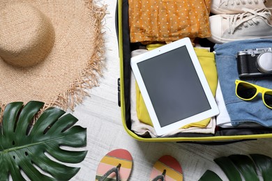 Packed suitcase with tablet and travel accessories on floor, flat lay. Summer vacation