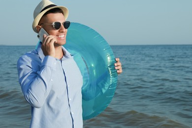 Happy man with inflatable ring talking by mobile phone near sea on beach. Business trip